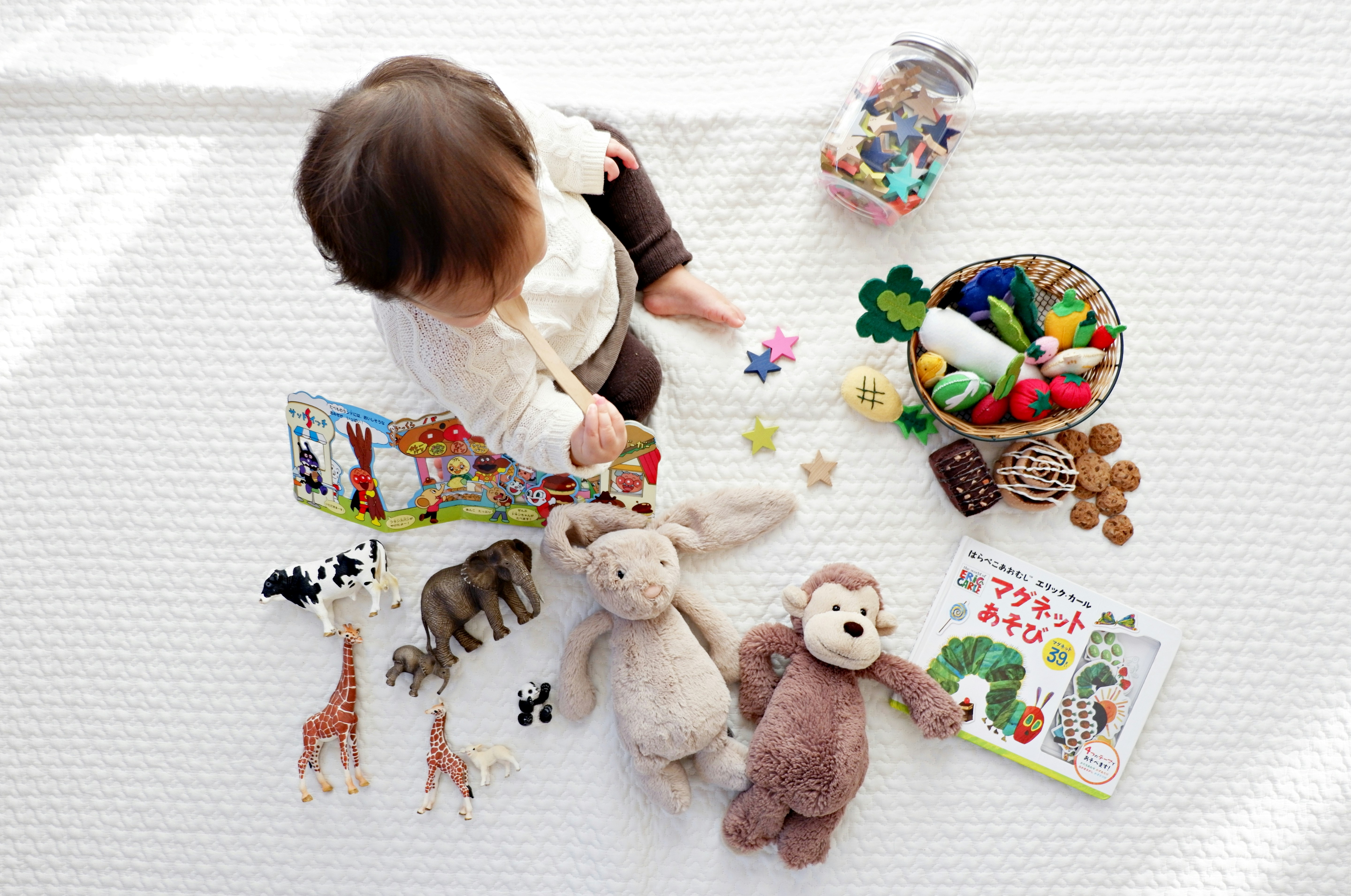 Image taken from above of young child on a white carpet surrounding by toys